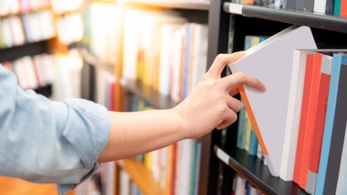 An arm reaching out to a bookshelf and pulling out a white resource binder