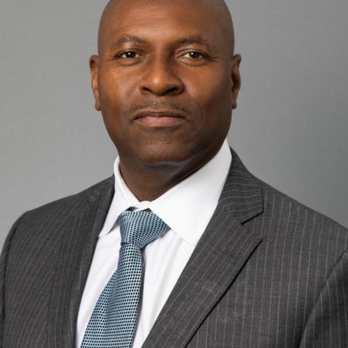 Nayland Smith headshot, in a grey suit and white shirt with a soft blue tie