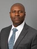 Nayland Smith headshot, in a grey suit and white shirt with a soft blue tie