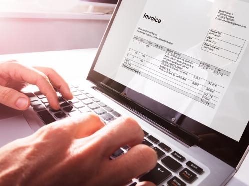 Hands typing on a keyboard with a screen showing an Invoice PDF