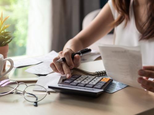 Young woman checking bills, taxes, bank account balance and calculating expenses in the living room at home